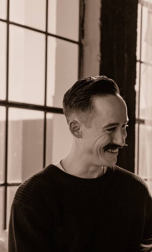 Sam, owner of Mural City Web Design, smiling beside a factory window